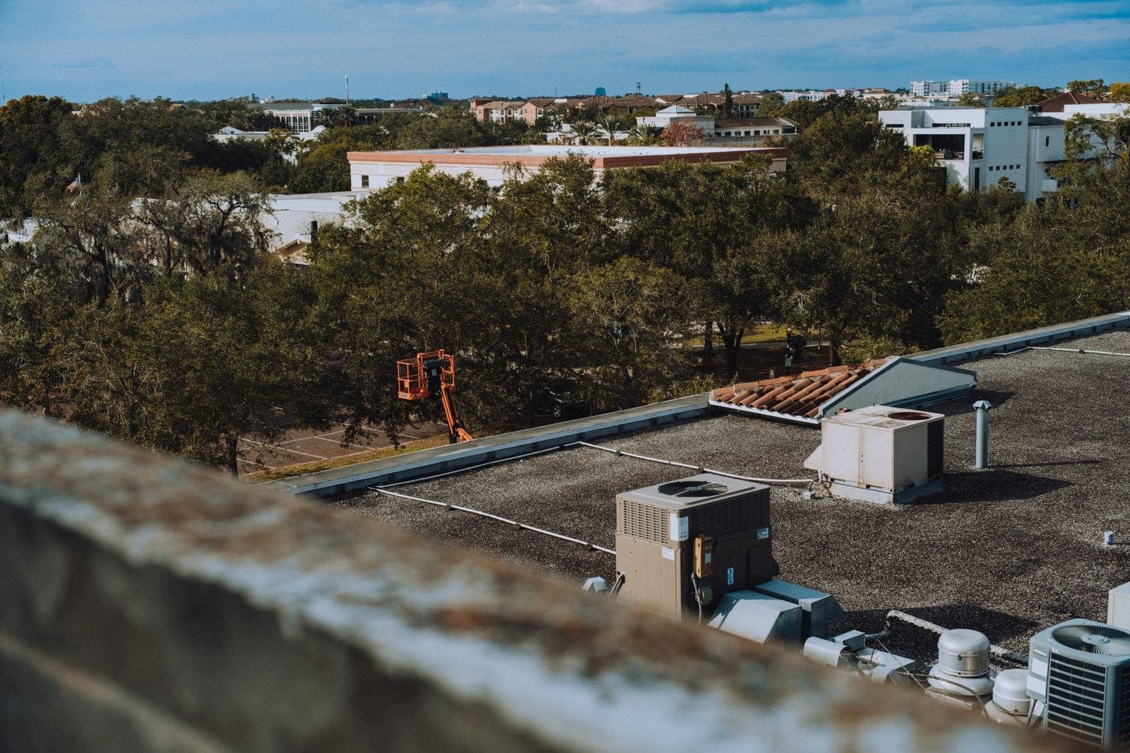Flat commercial rooftop with HVAC units and trees beyond