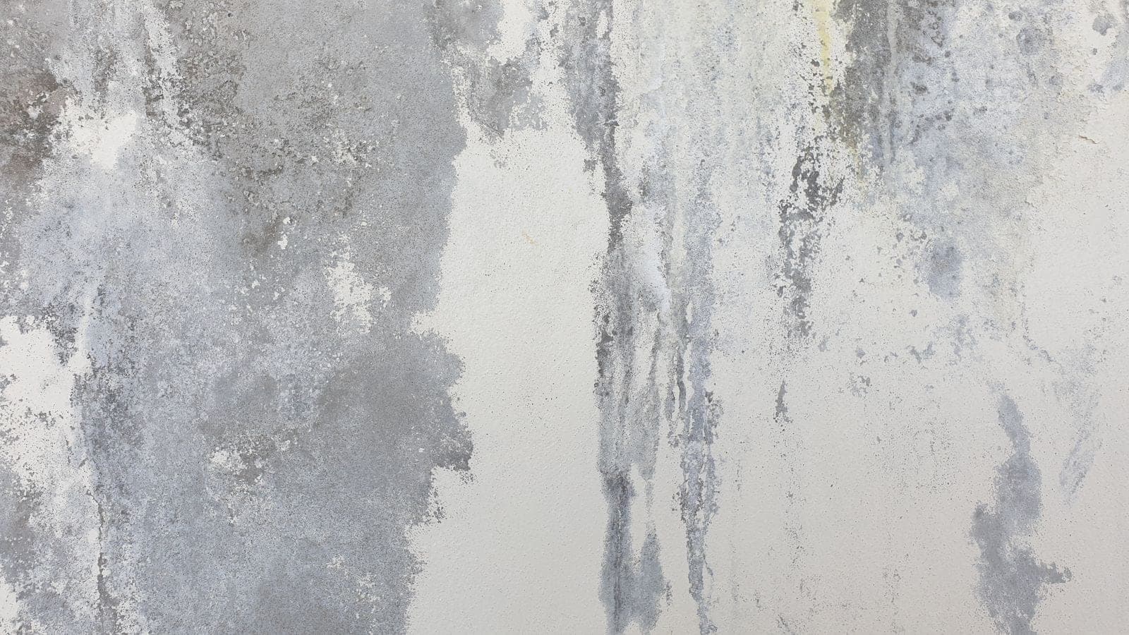 Water stains and streaks running down a white wall below a roof leak