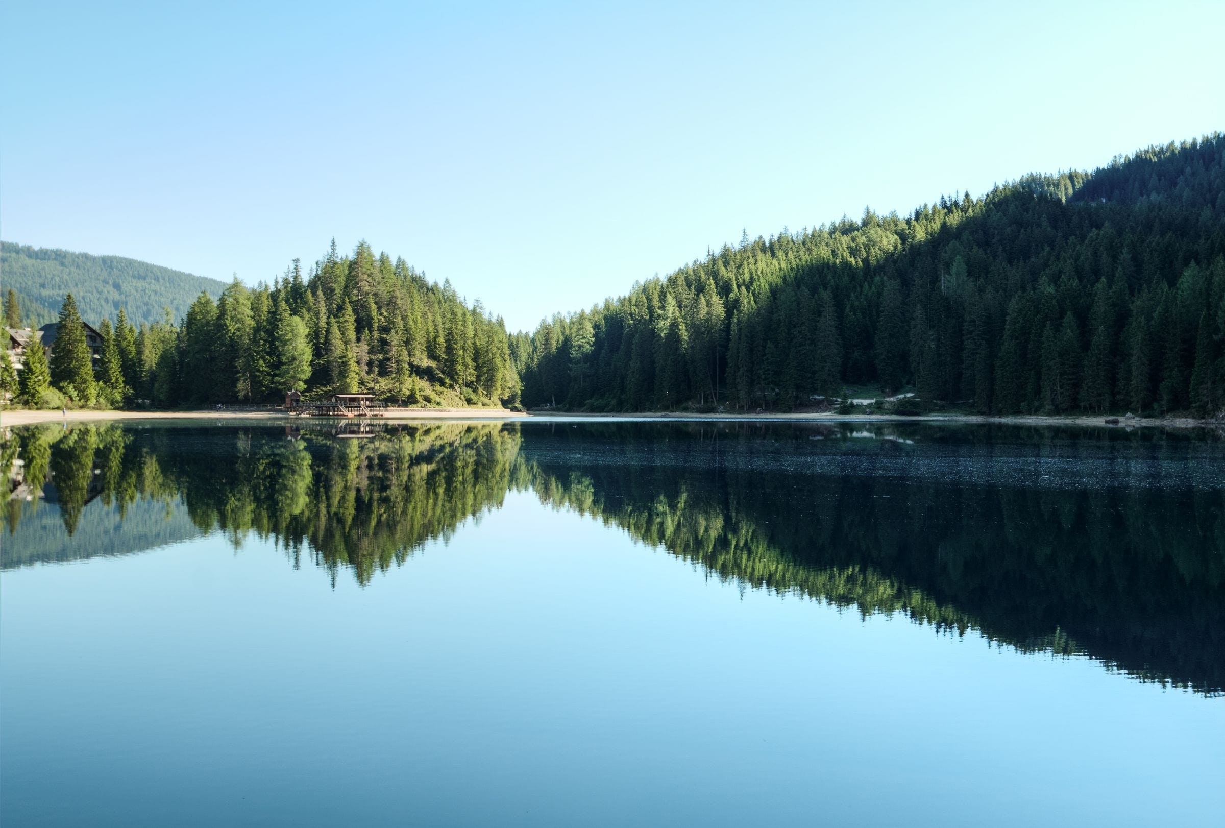 Calm lake reflecting pine-covered hills under a clear sky