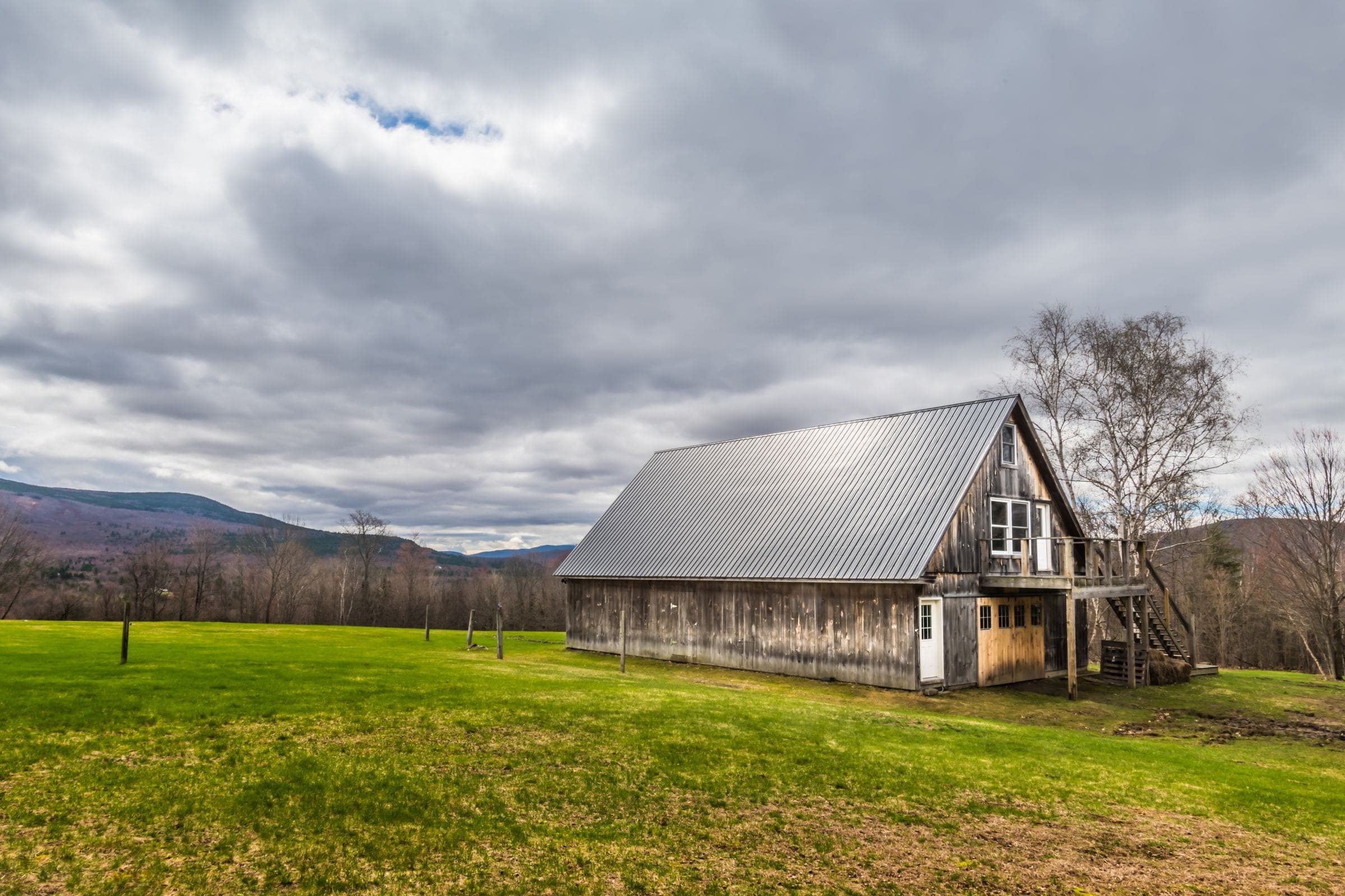 Weathered barn with a metal roof in a green field near hills