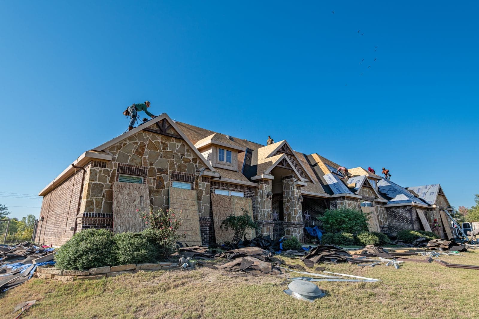 Roofers stripping the old roof from a large stone house