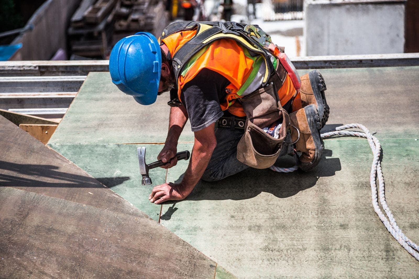 Roofer in a blue hard hat hammering on roof underlayment