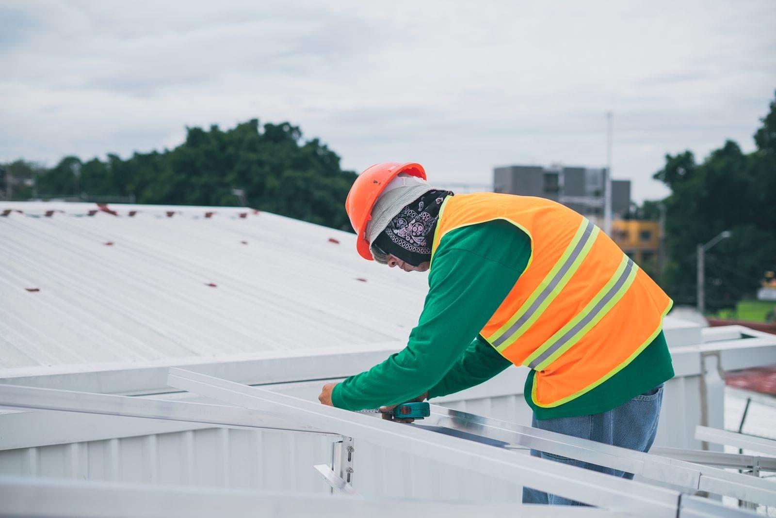 Roofer in a safety vest working on a white metal roof