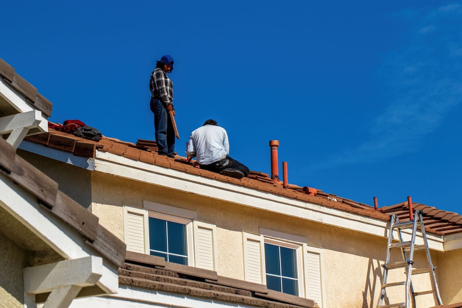 Two roofers at a ladder by the eave doing a roof inspection on a house
