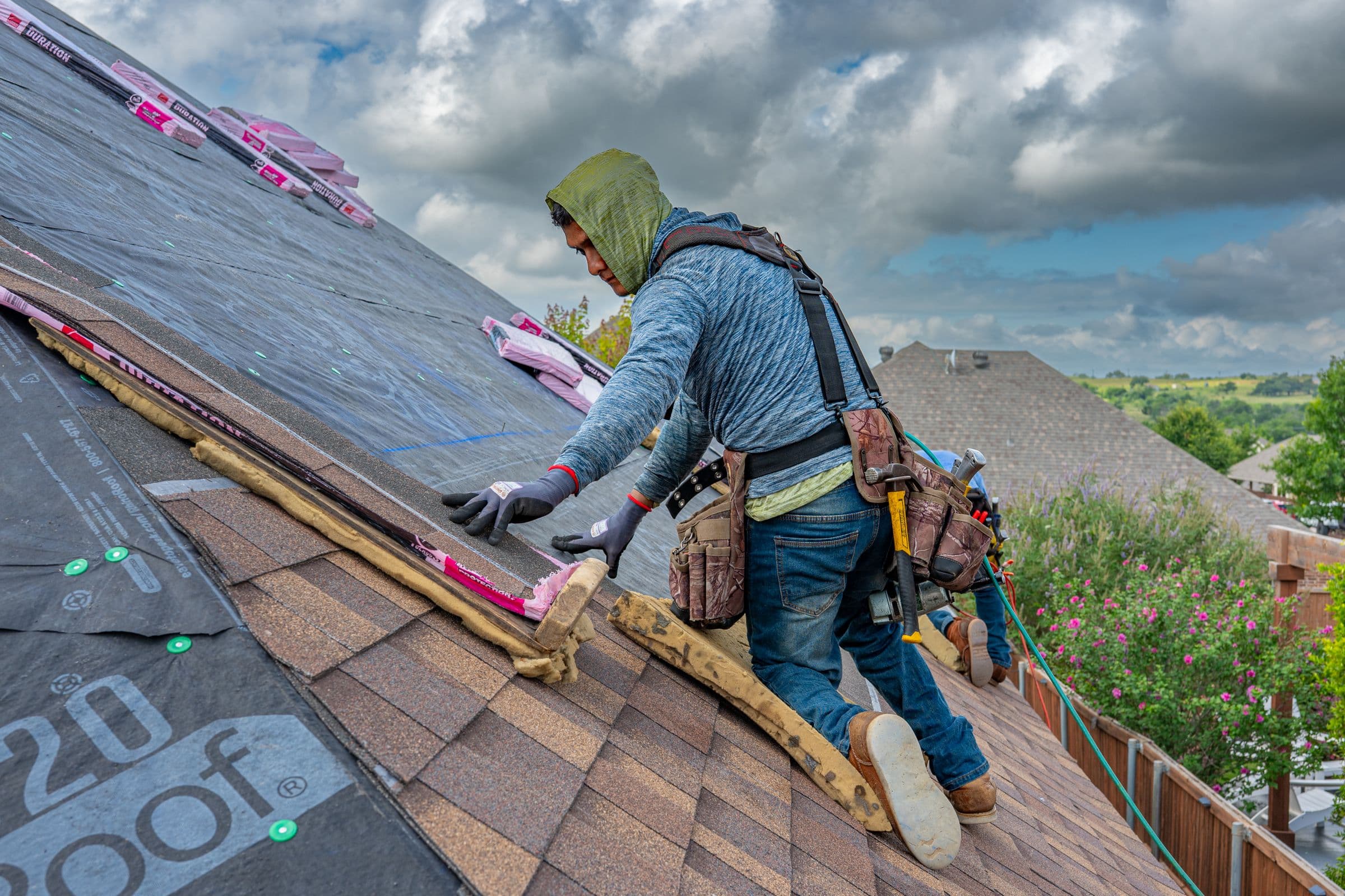 Roofer in a safety harness nailing asphalt shingles over new underlayment