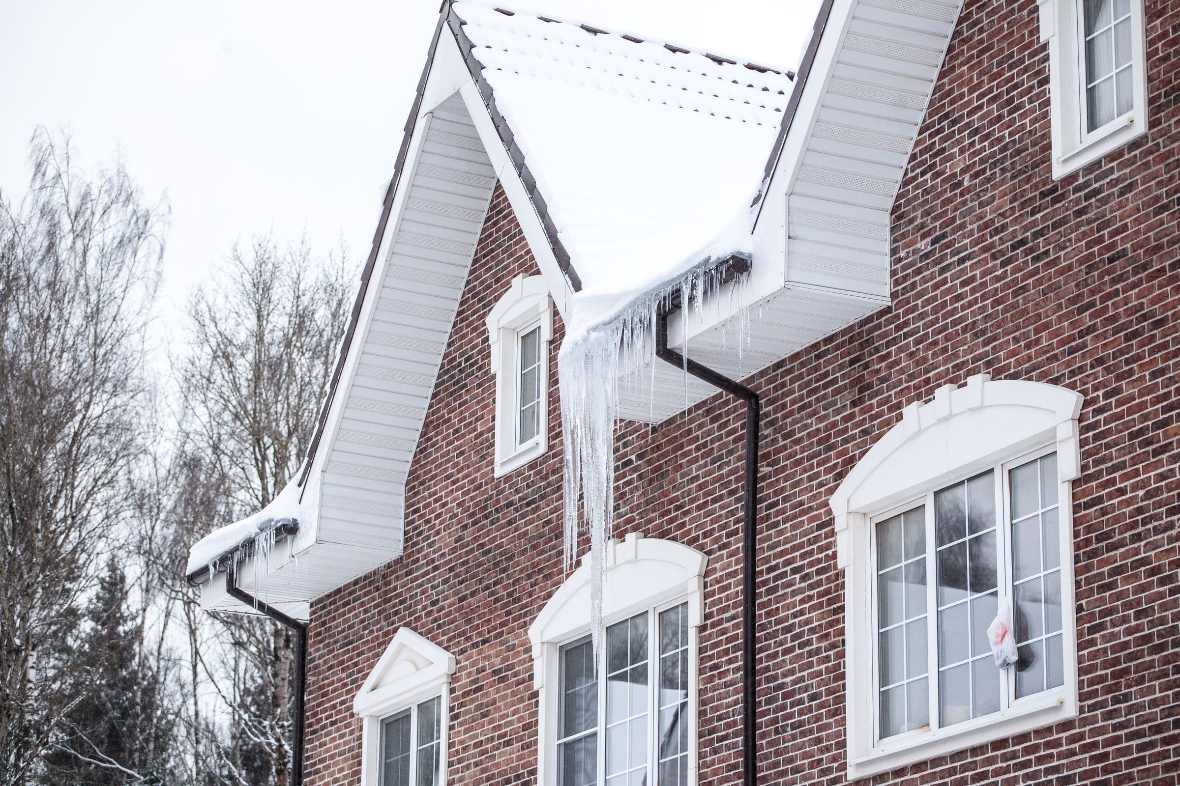 Brick house with ice and icicles along the gutters and gables, waiting on ice dam removal
