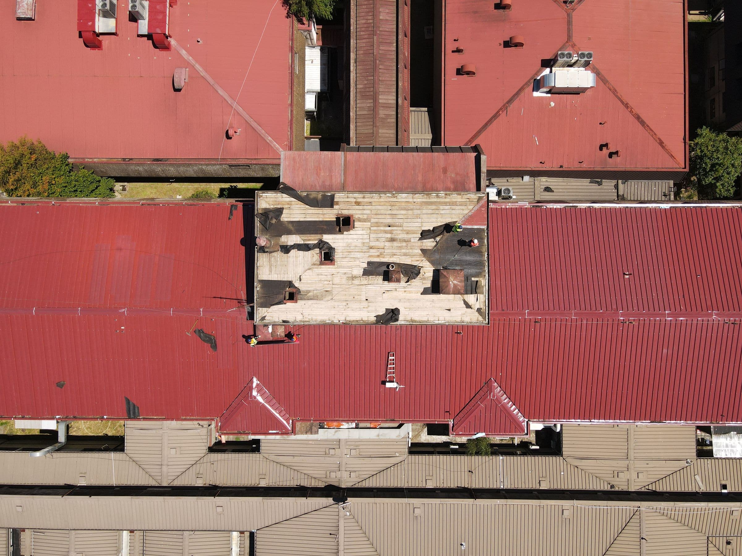 Aerial view of a red metal roof with a section torn open, a typical storm damage roof repair job