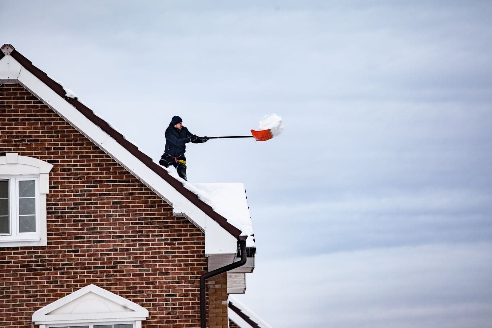 Man shoveling snow off a steep house roof